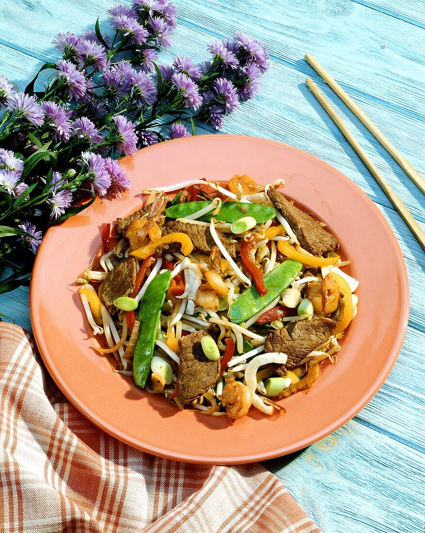 Rinder-Chop-Suey mit Gemüse auf Teller; Deko: Blumen,Stäbchen