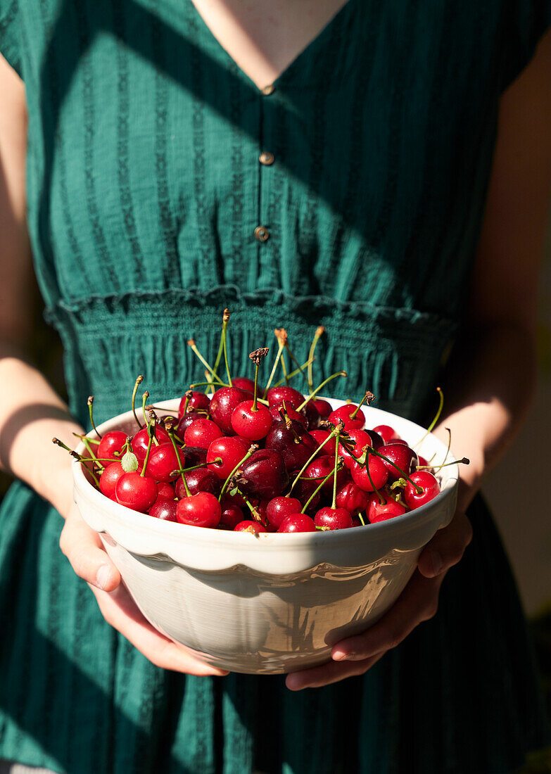 A woman holding a bowl of fresh cherries