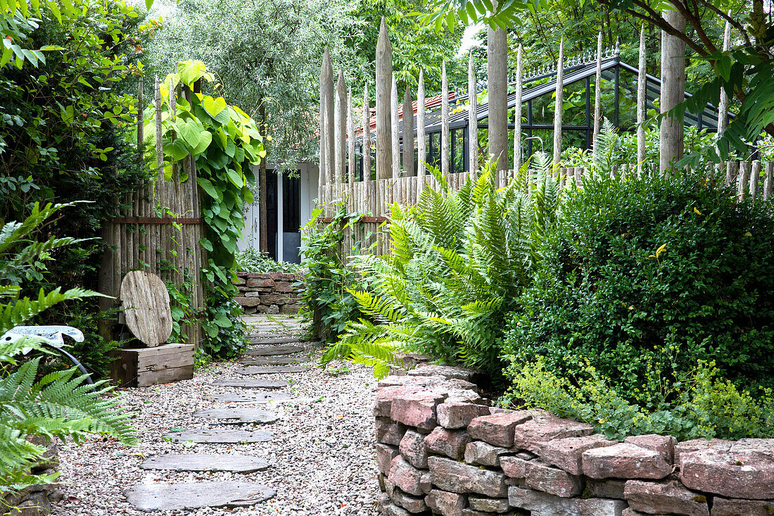 Dry stone wall and lush planting along the garden path, palisades of wooden posts in the background