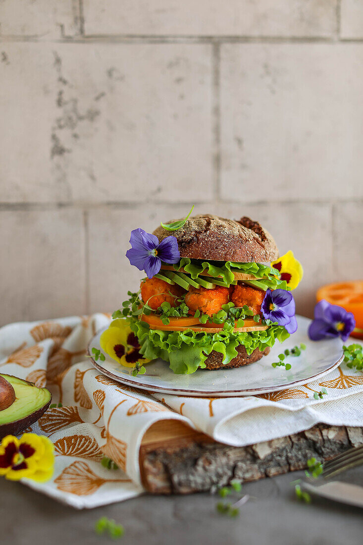 Homemade fish finger burger with avocado, lettuce leaves and edible flowers