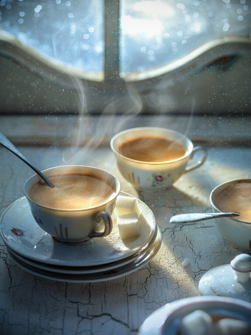 Steaming cups of coffee in front of a window