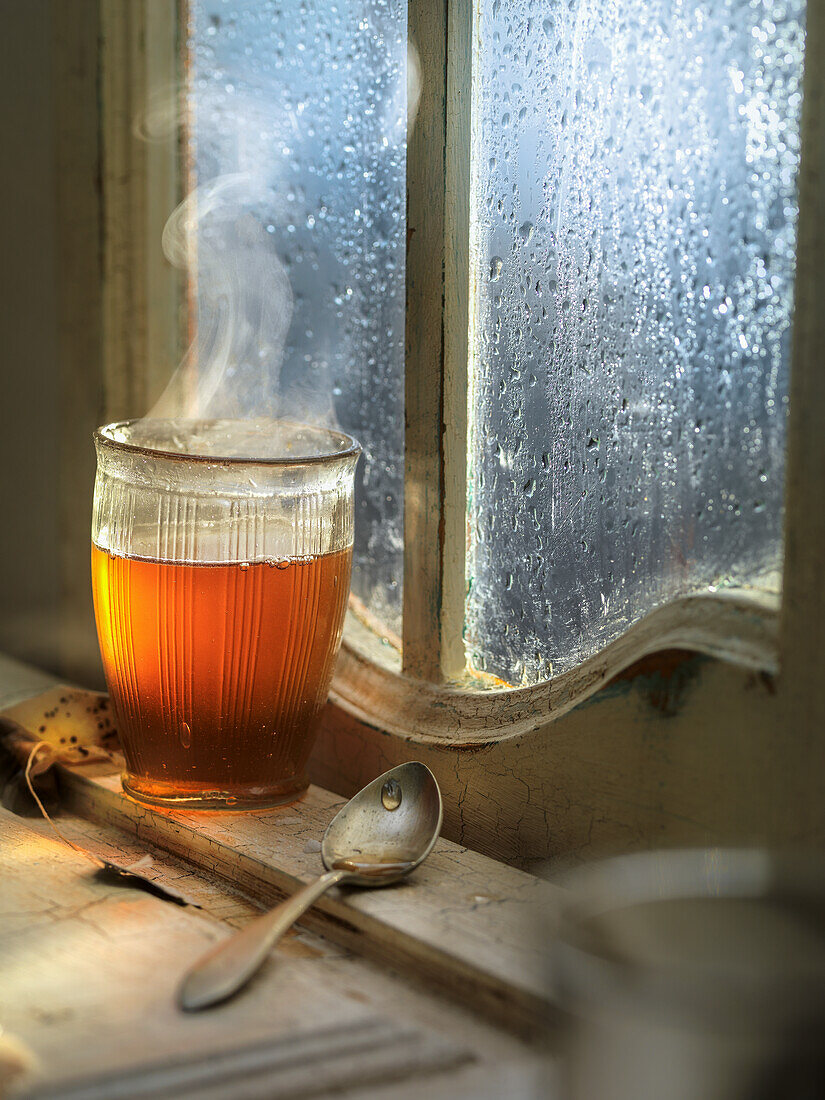 A steaming cup of tea in a glass in front of a window