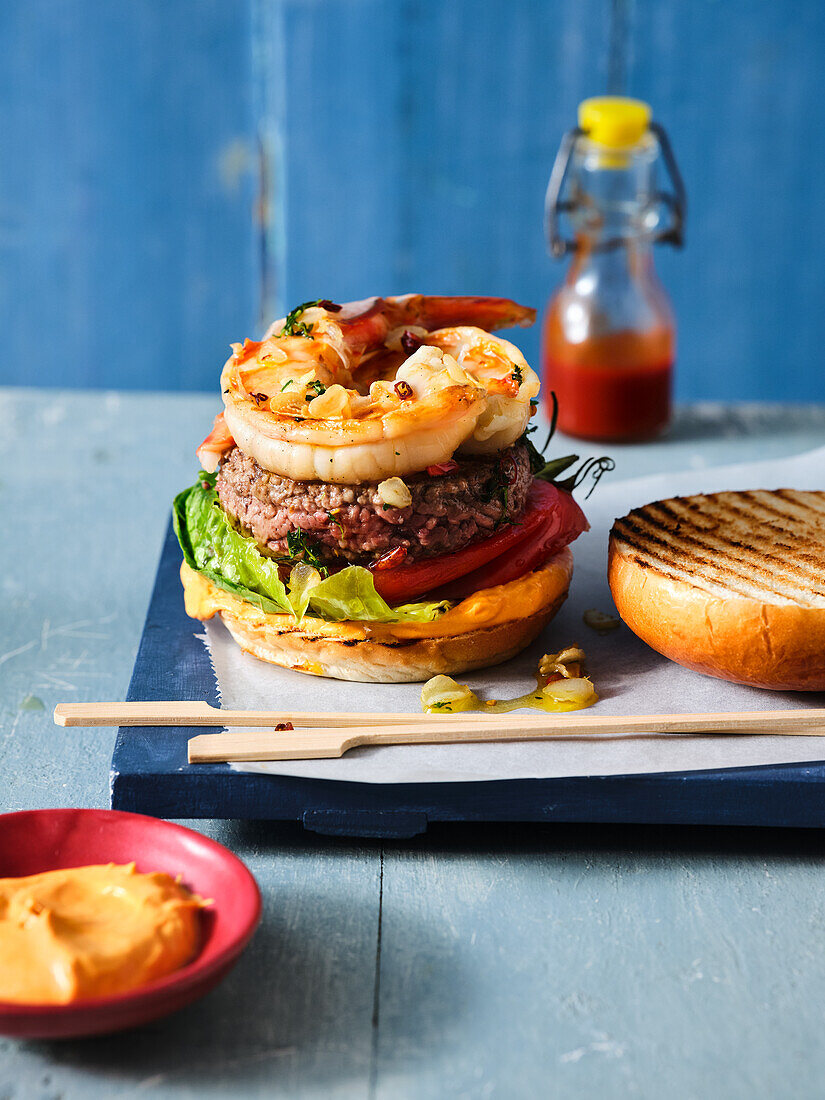 Burger with beef pattie, prawns, and shellfish and a dish of aioli