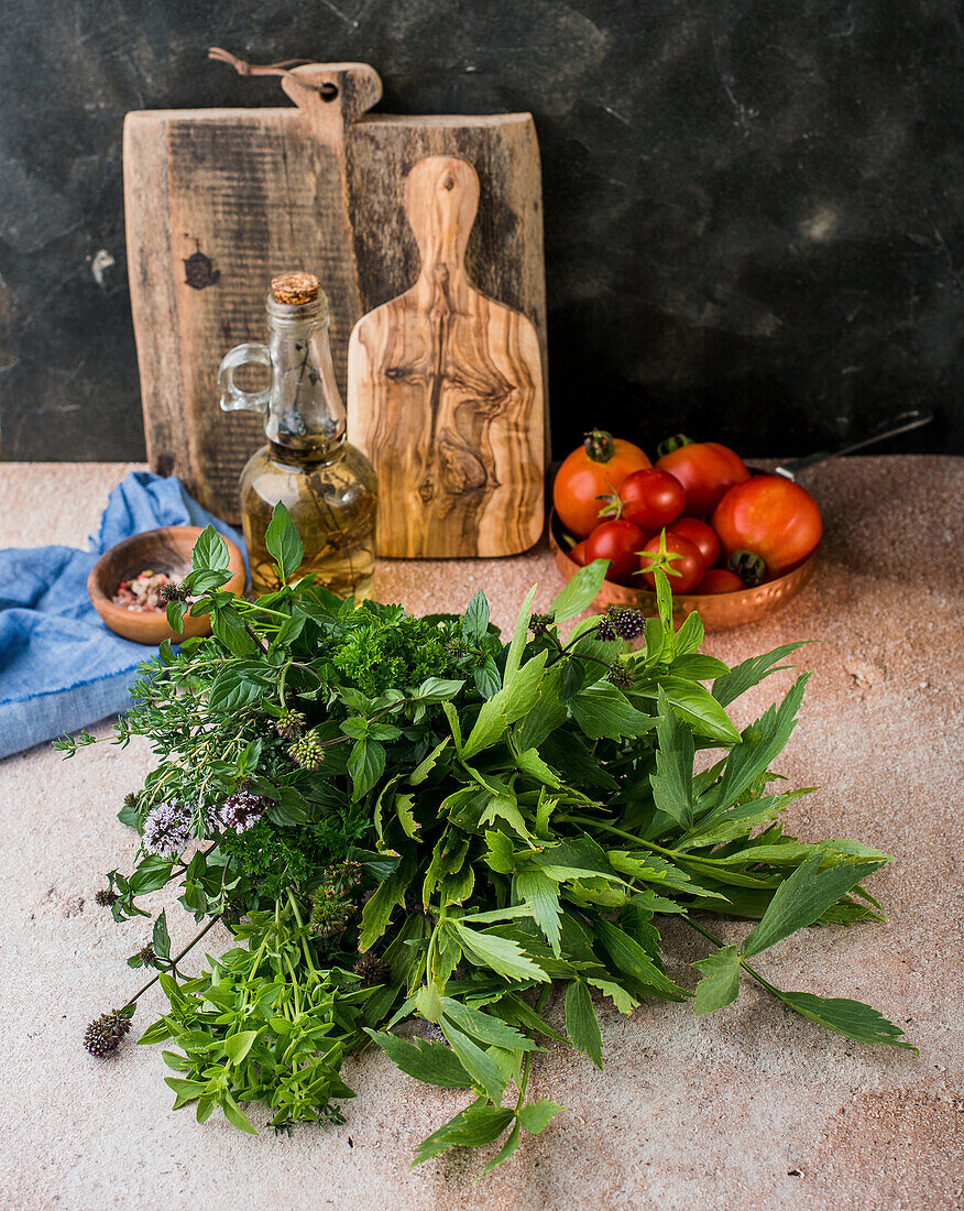 Fresh herbs, in the background tomatoes, herb oil, and cutting boards