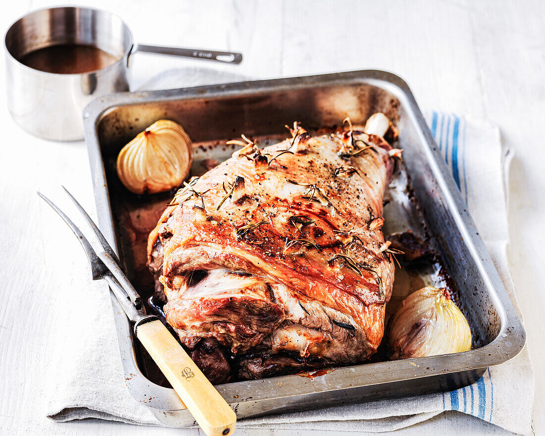 Roasted leg of lamb with roasted onions and rosemary in a roaster, served with sauce