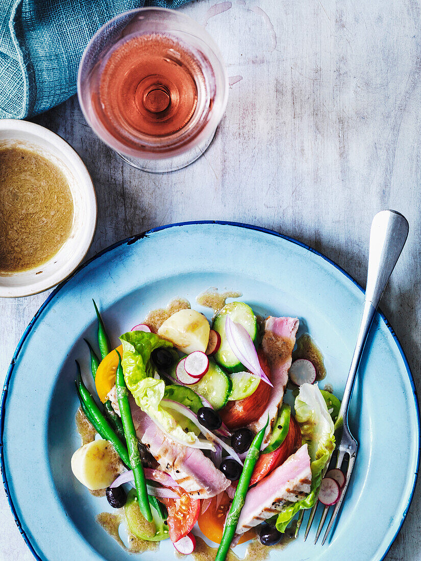 Salad Nicoise with dressing served with a glass of rosé wine