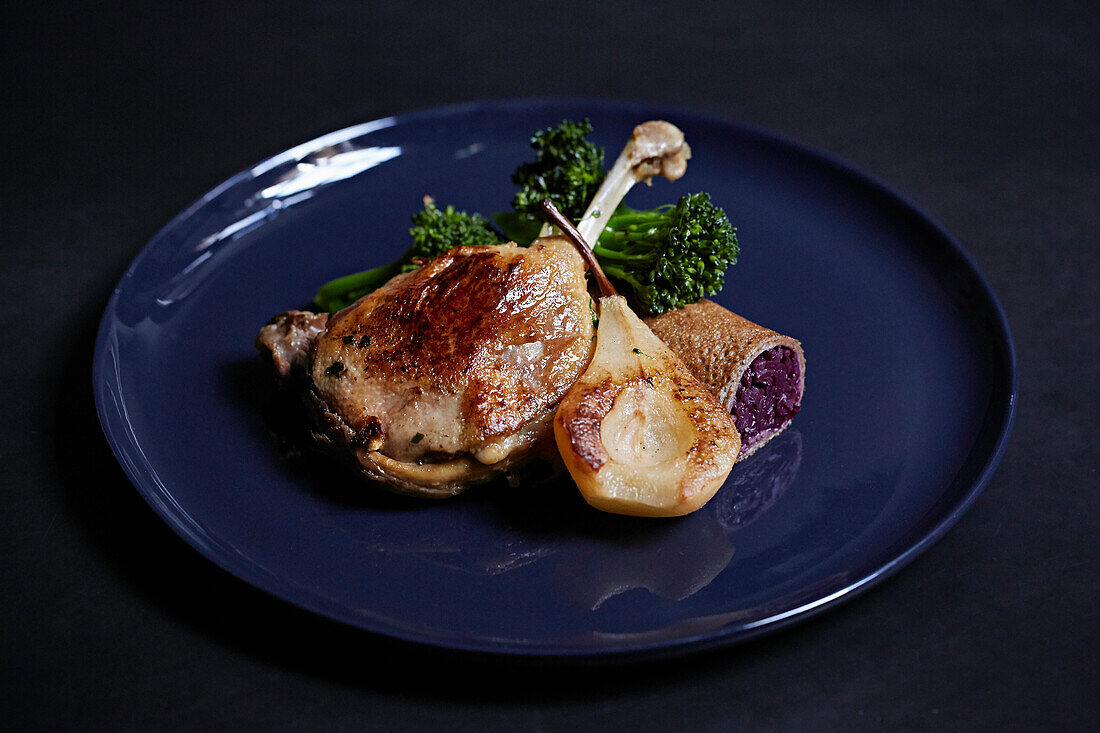 Duck leg served with pear on a blue plate