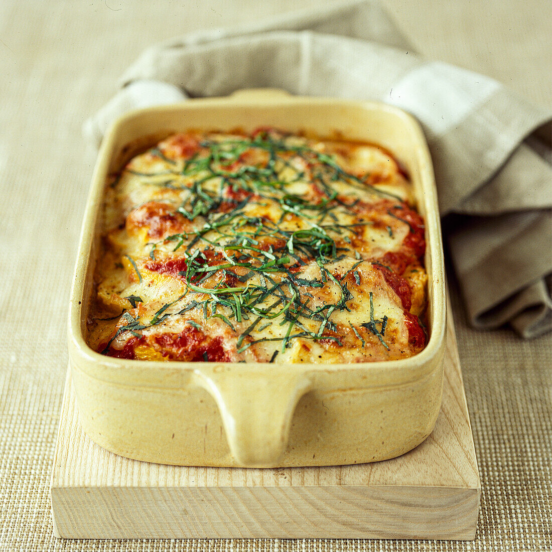Zucchini parmigiana in a casserole dish with basil strips