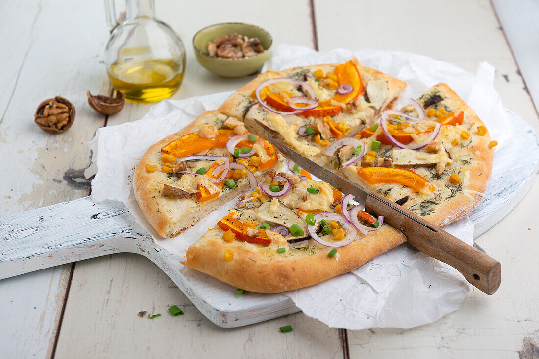 Vegane Pizza mit Kräutercreme, Hokkaido-Kürbis, Steinplizen, Mais, Zwiebeln und Walnüssen
