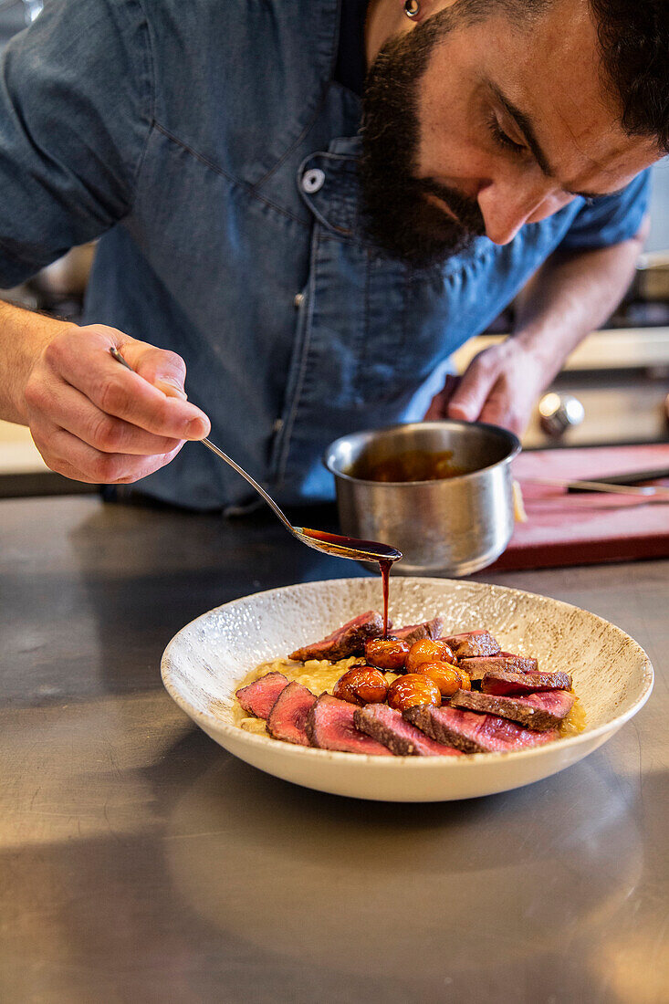 Crop Caucasian chef pouring sauce on beef in bowl at commercial kitchen