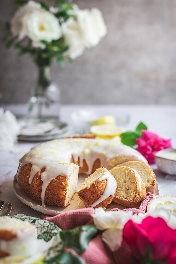 Sponge lemon cake on a table next to white and pink roses with petals