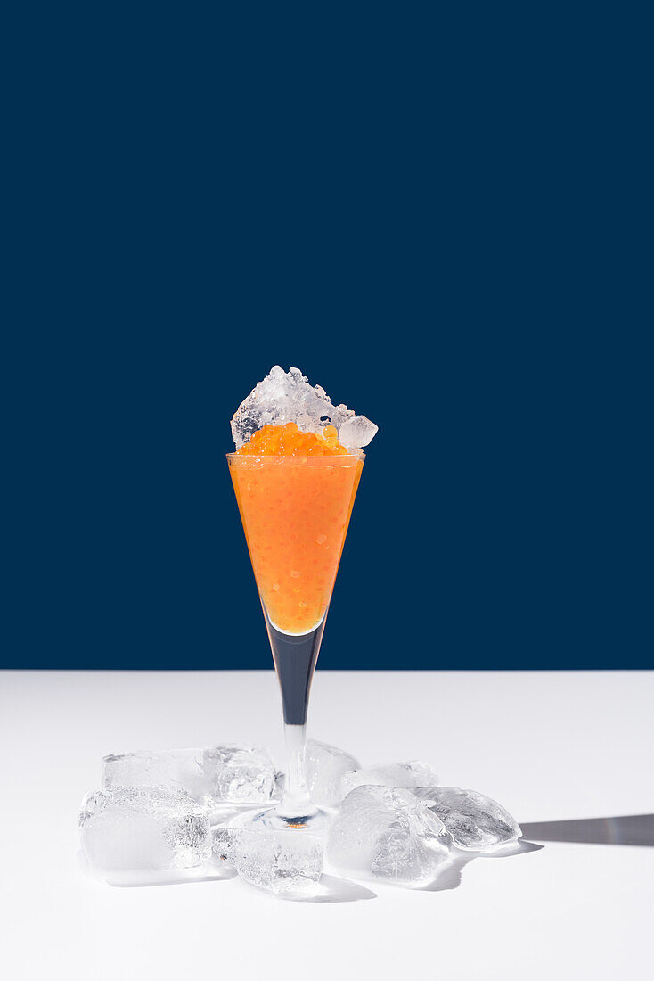 Orange tobiko caviar placed on cocktail glass with ice on white and blue background