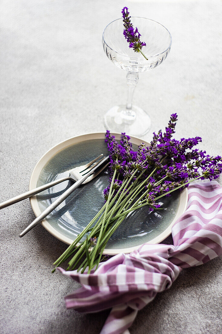 Sommerliches Gedeck mit Lavendelblüten und gestreifter Stoffserviette auf Betontisch