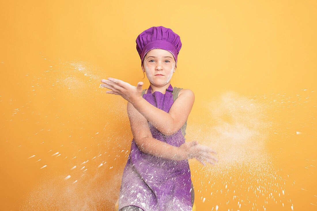 Mädchen in lila Kochkleidung klatscht mit Mehl in die Hände
