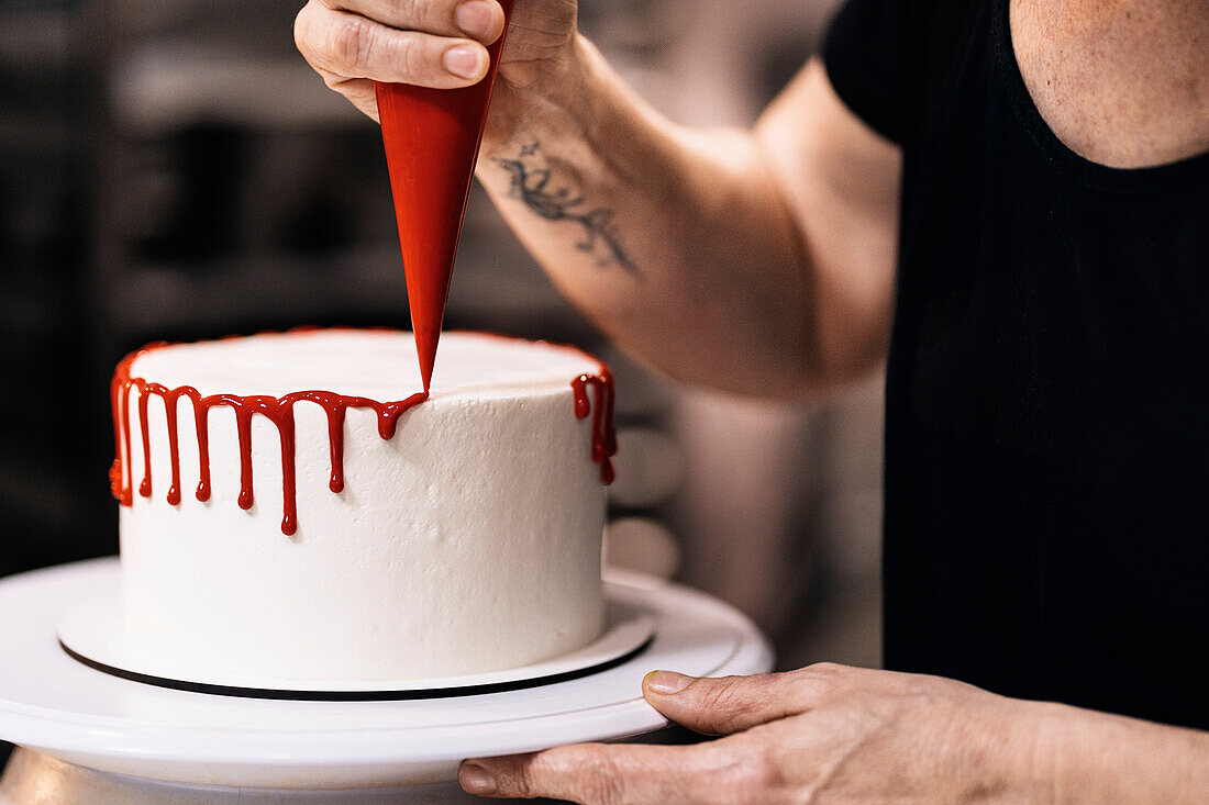 Unrecognizable woman spinning plate with delicious cake and squeezing red icing from pastry bag during work in bakery