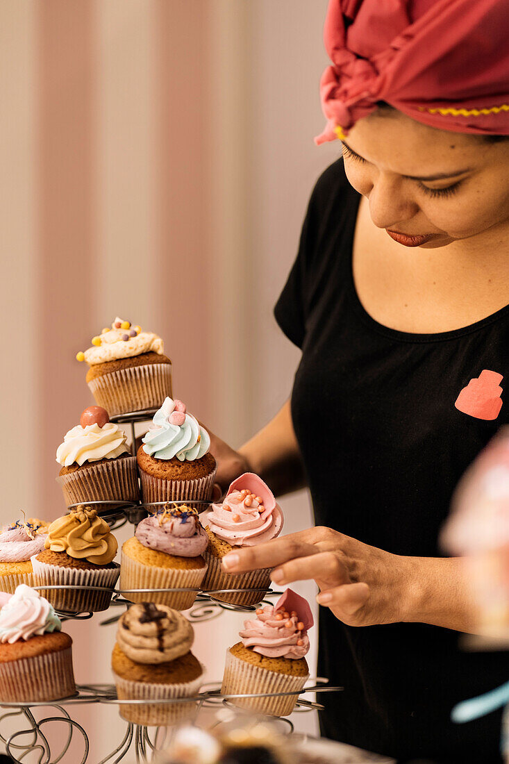 Hispanic woman in headscarf arranging desserts on table while working in bakery in daytime