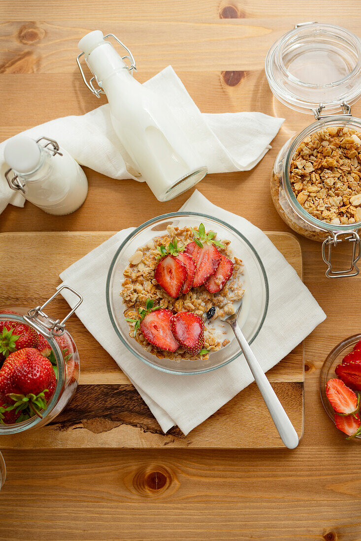 Glass bowl of delicious healthy granola with milk and fresh sliced strawberries served on wooden table