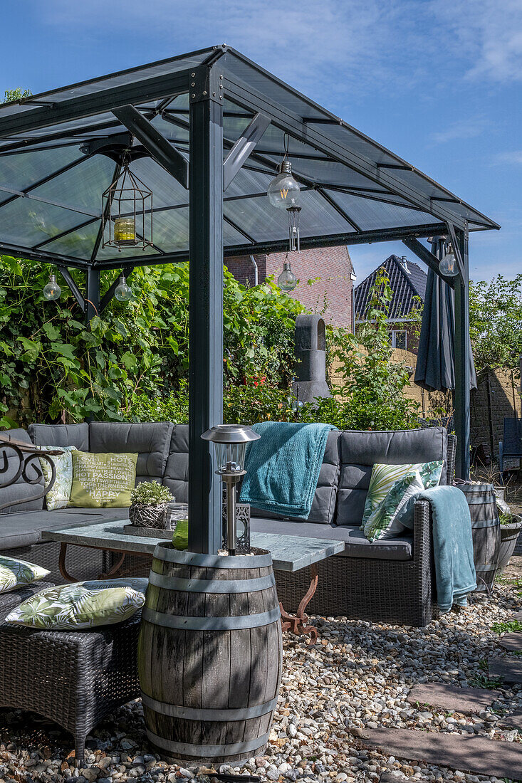 Outdoormöbel unter grauer Pergola, mit alten Regentonnen als Stützfüße