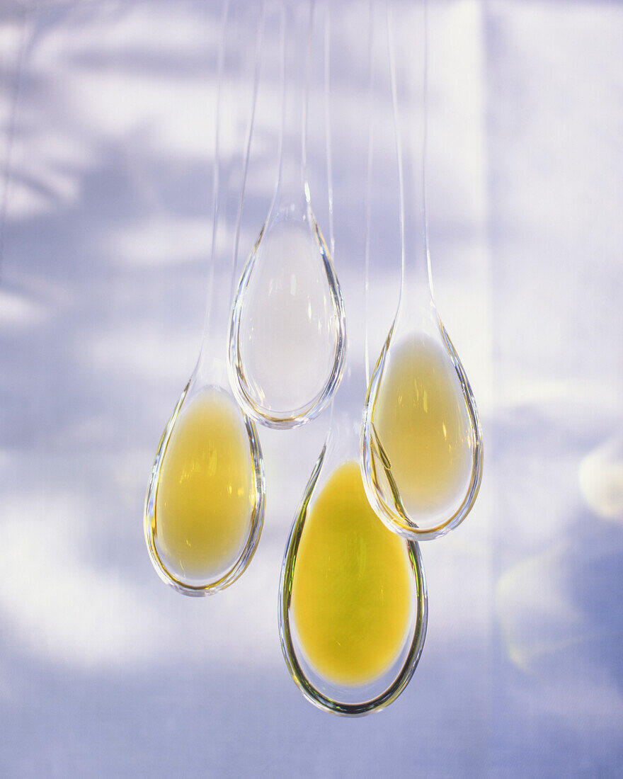 Four transparent spoons with cooking oils