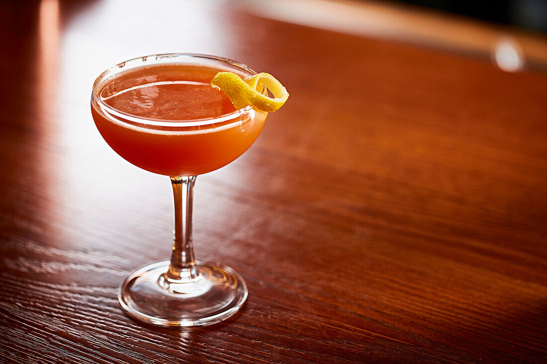 Orange cocktail with lemon peel garnish on a wooden table