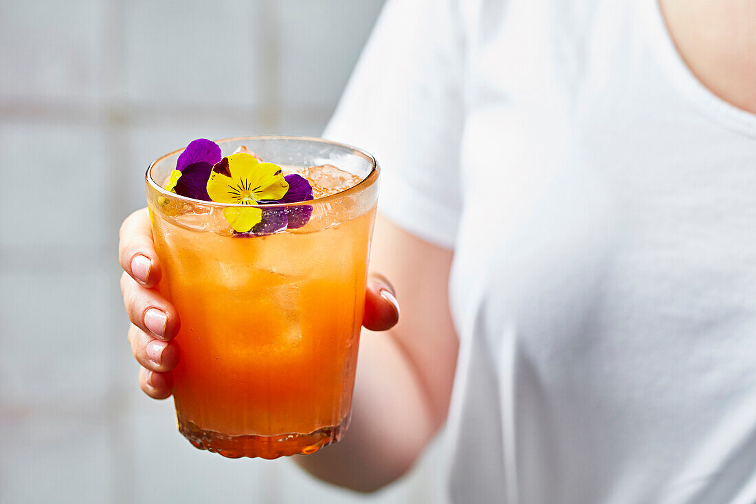 Orange summer cocktail garnished with edible flowers