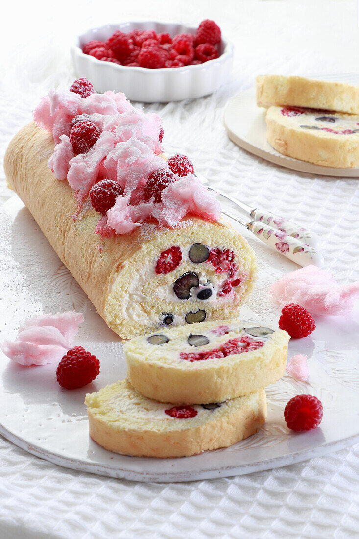 Biskuitroulade mit frischen Beeren, dekoriert mit Zuckerwatte