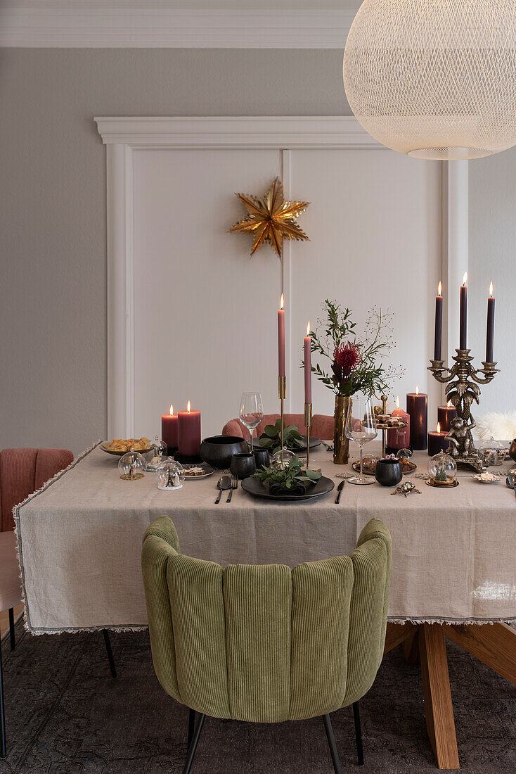 Festively laid Christmas table with candles, velvet upholstered chairs around the table