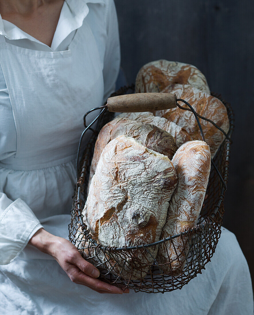 A woman holding a wire basket of freshly baked bread
