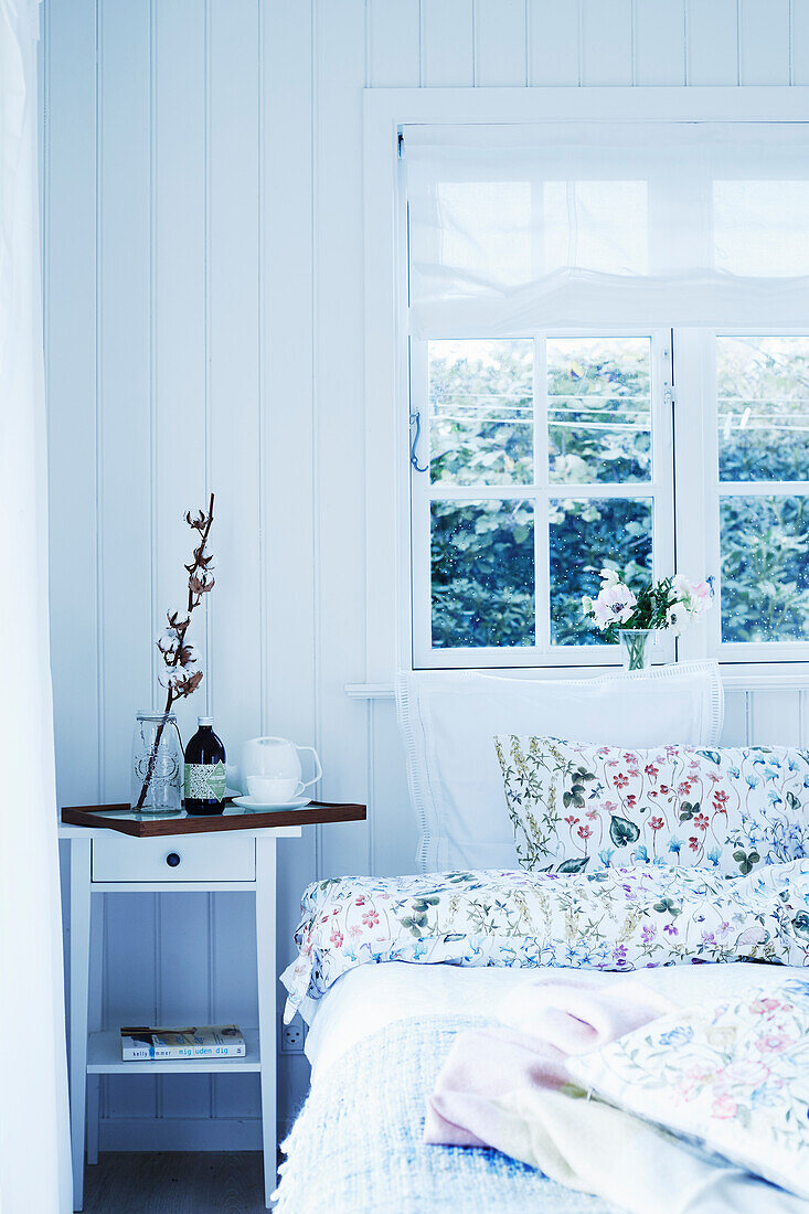 Double bed with floral, springtime bed linen; tray with twig in vase on bedside table