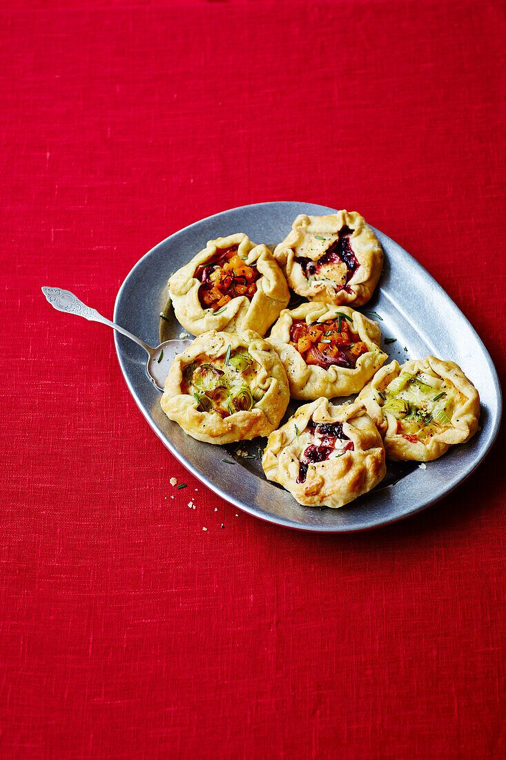 Hearty tartlets with different fillings on a silver plate and red background