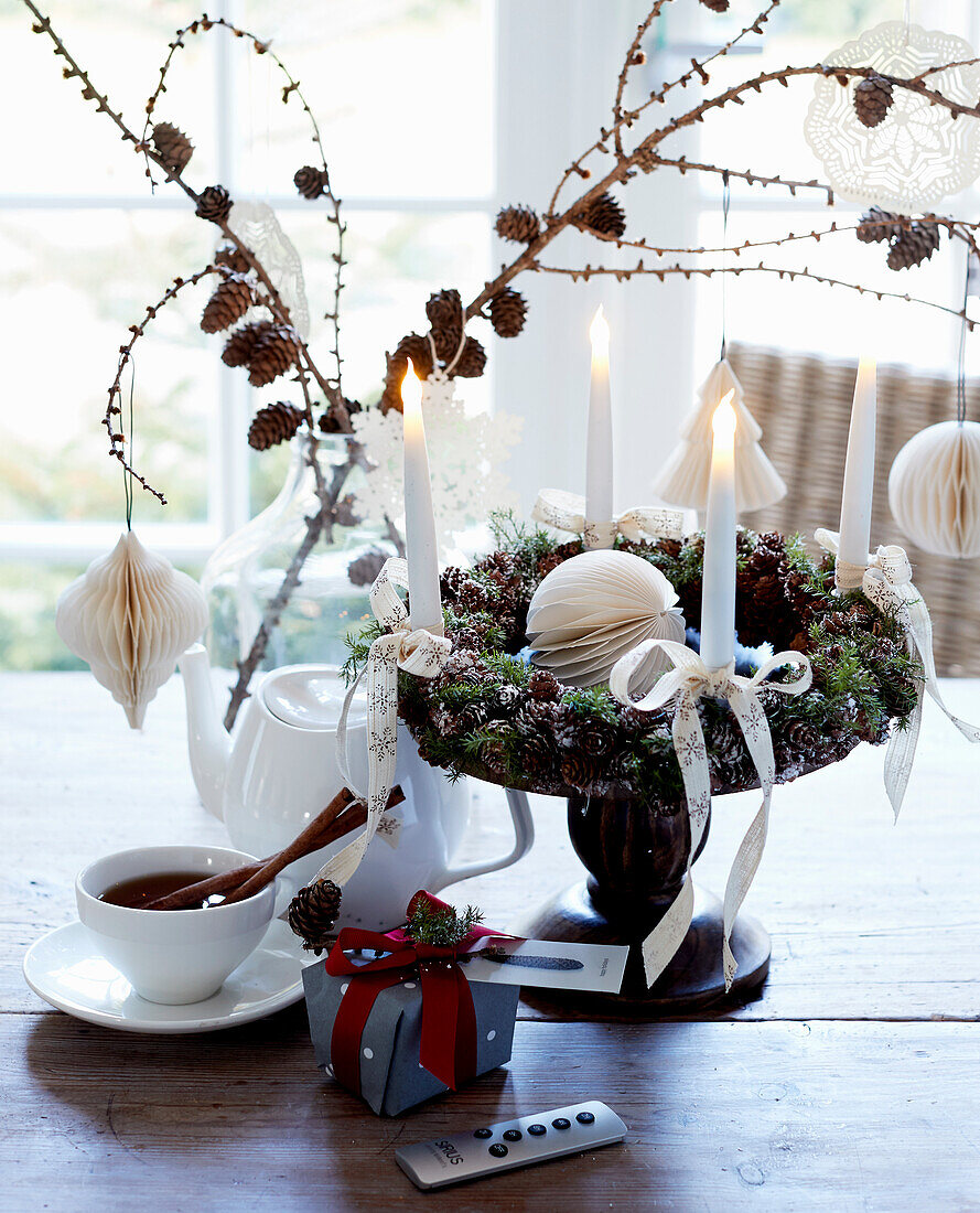 Adventskranz mit weißen Kerzen und Lärchenzweige in Ballonflasche auf Holztisch