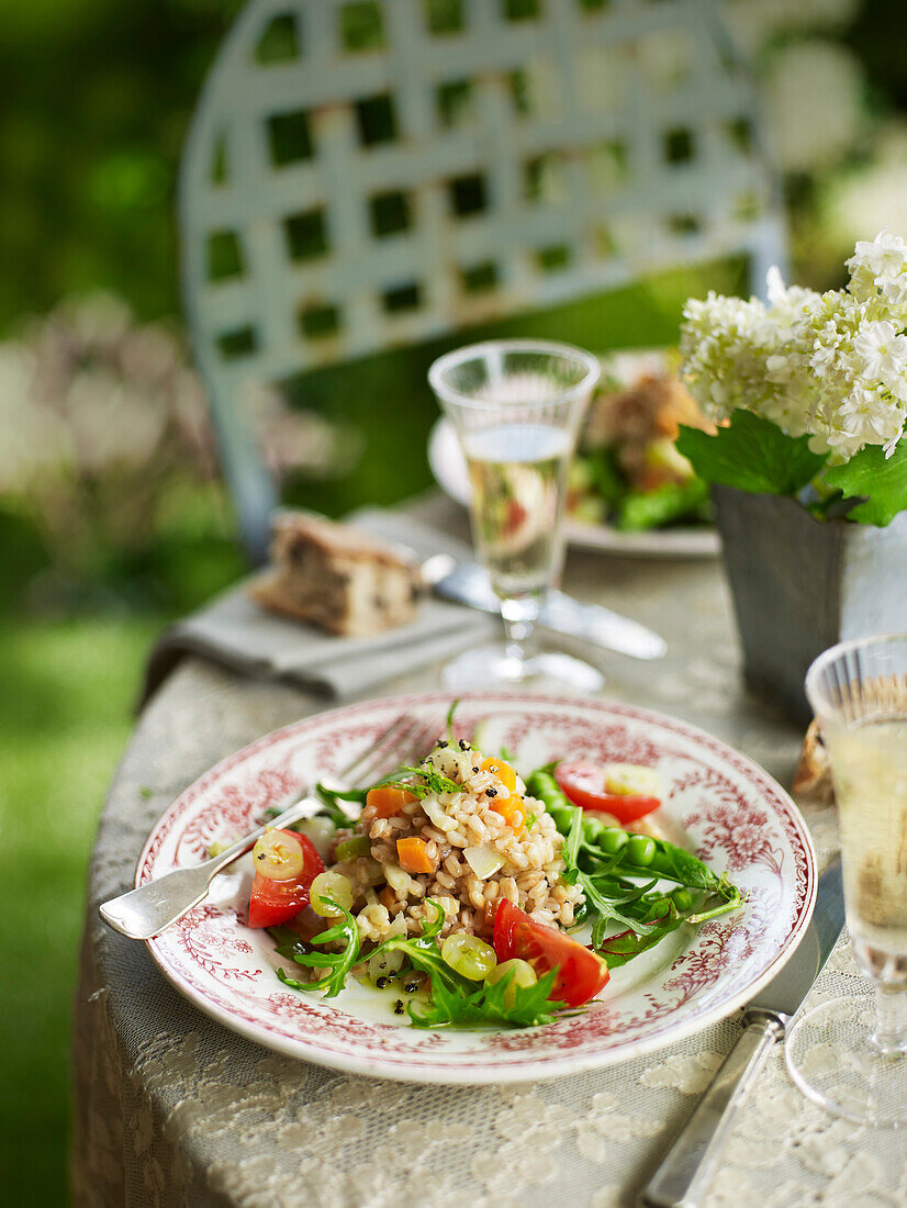 Dinkelsalat mit Erbsen und Stachelbeeren auf sommerlichem Tisch im Garten