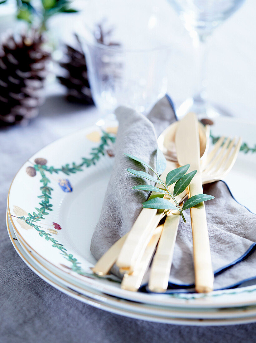 Christmas place setting with gold-coloured cutlery and evergreen sprig