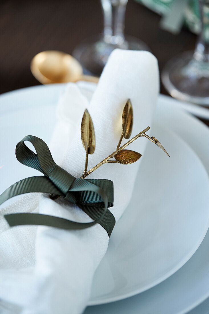White place setting with green decorative ribbon as napkin ring and golden twig