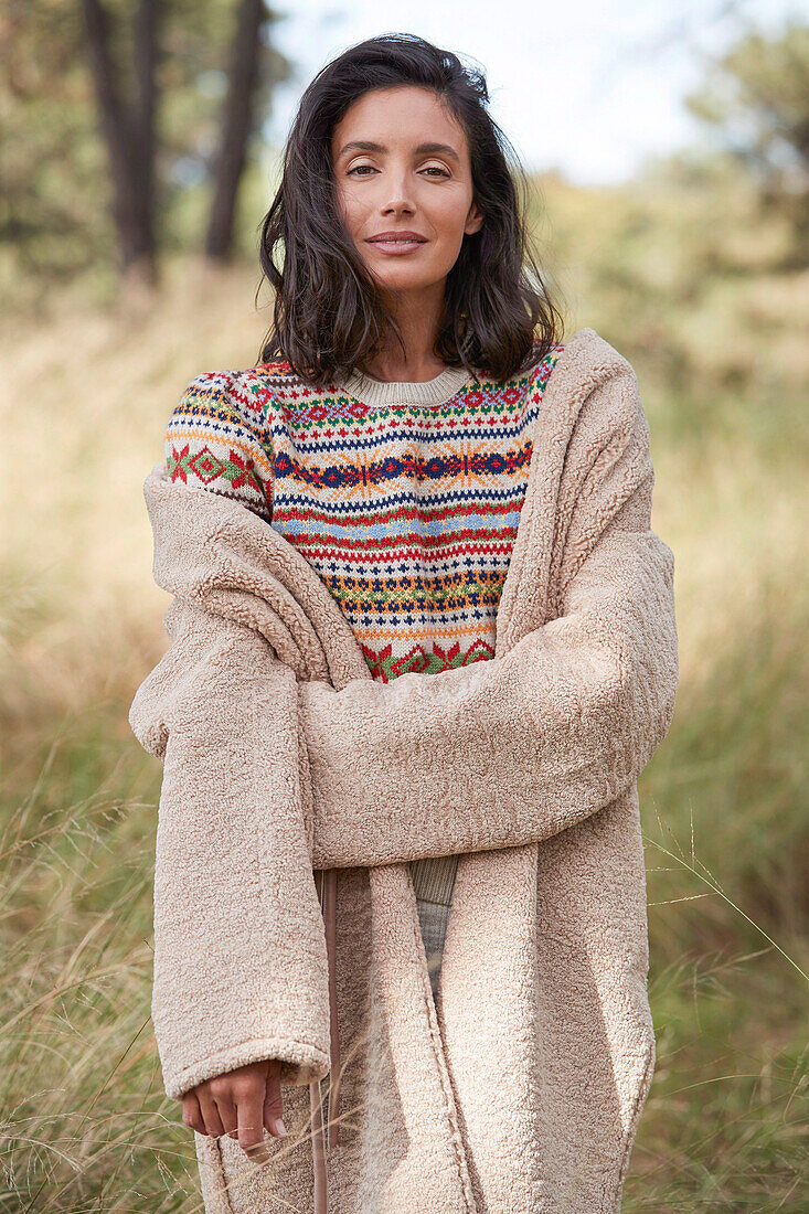 A brunette woman outside wearing a knitted jumper and a dusty pink coat