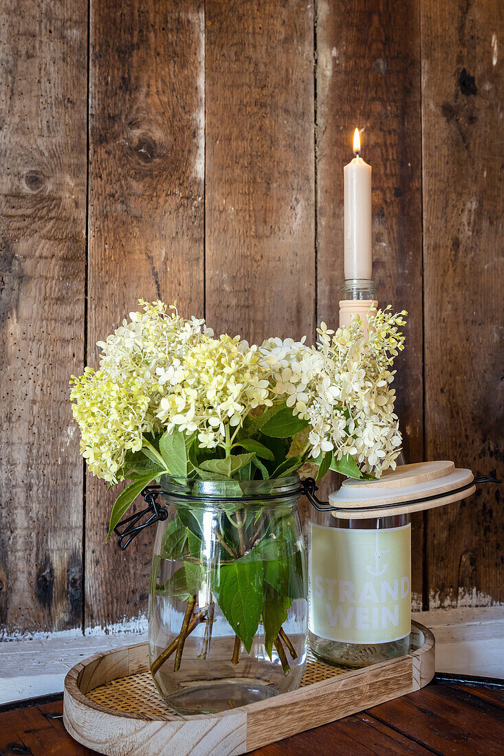 Weisse Hortensien in einer Vase, Flasche mit Kerze im Hintergrund, Etikett Strandwein