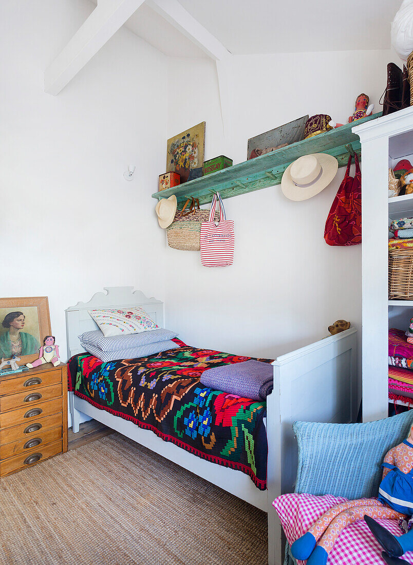 Bed with colourful bedspread, above it green shelf in white painted guest room