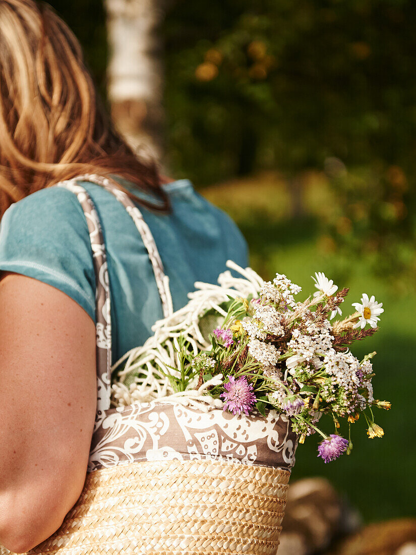 Frau trägt Korbtasche mit Wiesenblumen