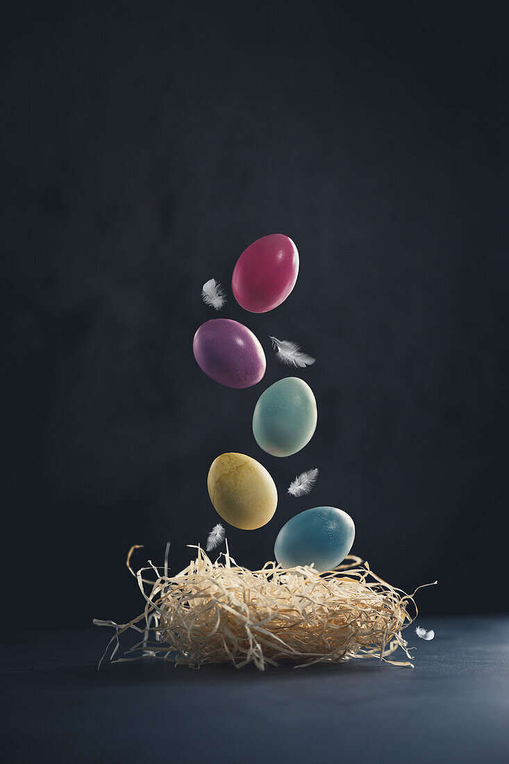 An Easter nest with floating coloured eggs and feathers