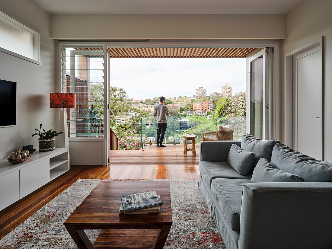 A living room with an upholstered sofa and a wooden coffee table with a view out onto a terrace