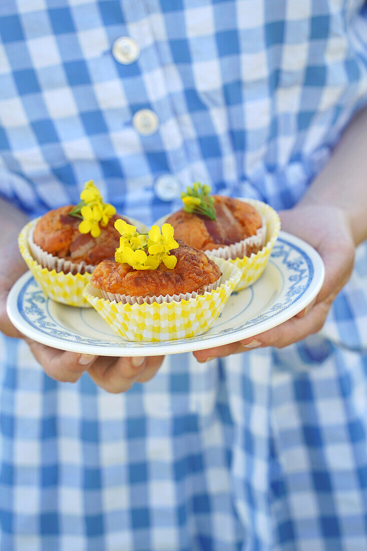 Frau hält Teller mit drei Muffins mit gelben Blüten in den Händen