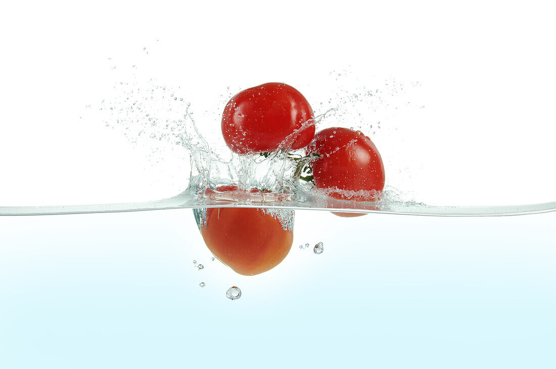 Three tomatoes splashing in water