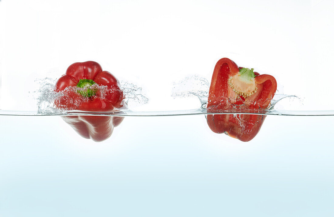 Two red peppers splashing in water