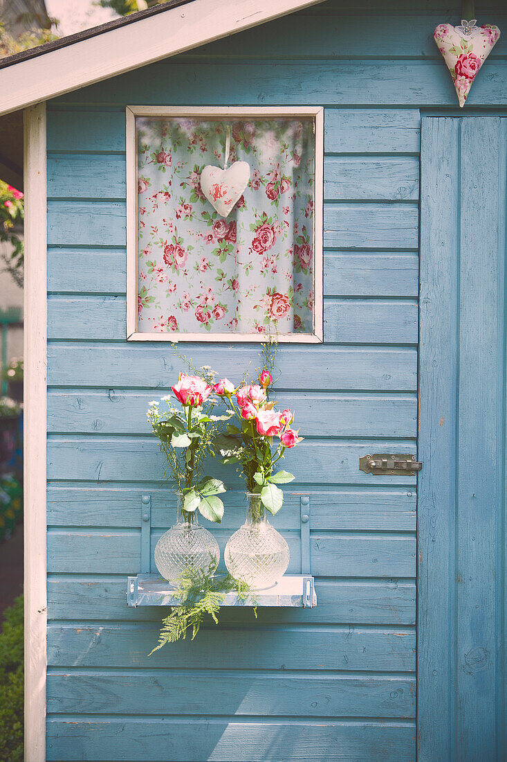 Blumenvasen mit Rosen an Gartenhaus