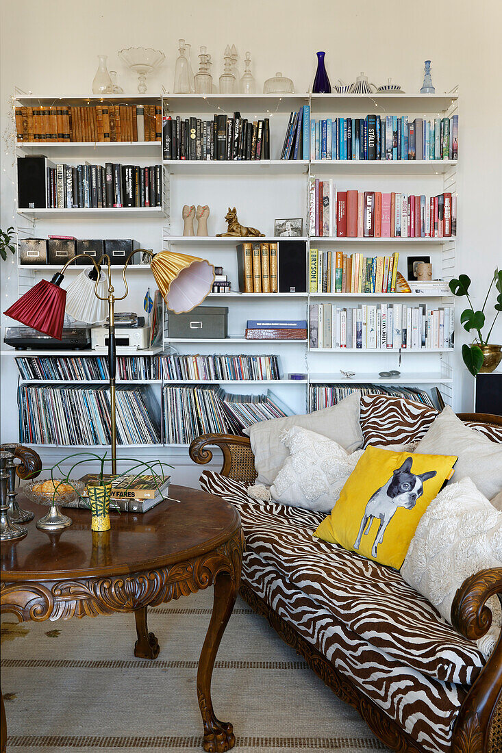 Reading corner with antique table and zebra print sofa in front of a wall of bookshelves