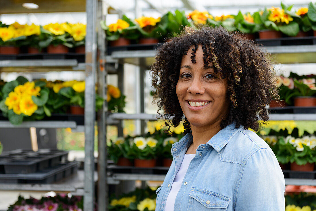 Smiling young woman in nursery in front of shelf with flower pots