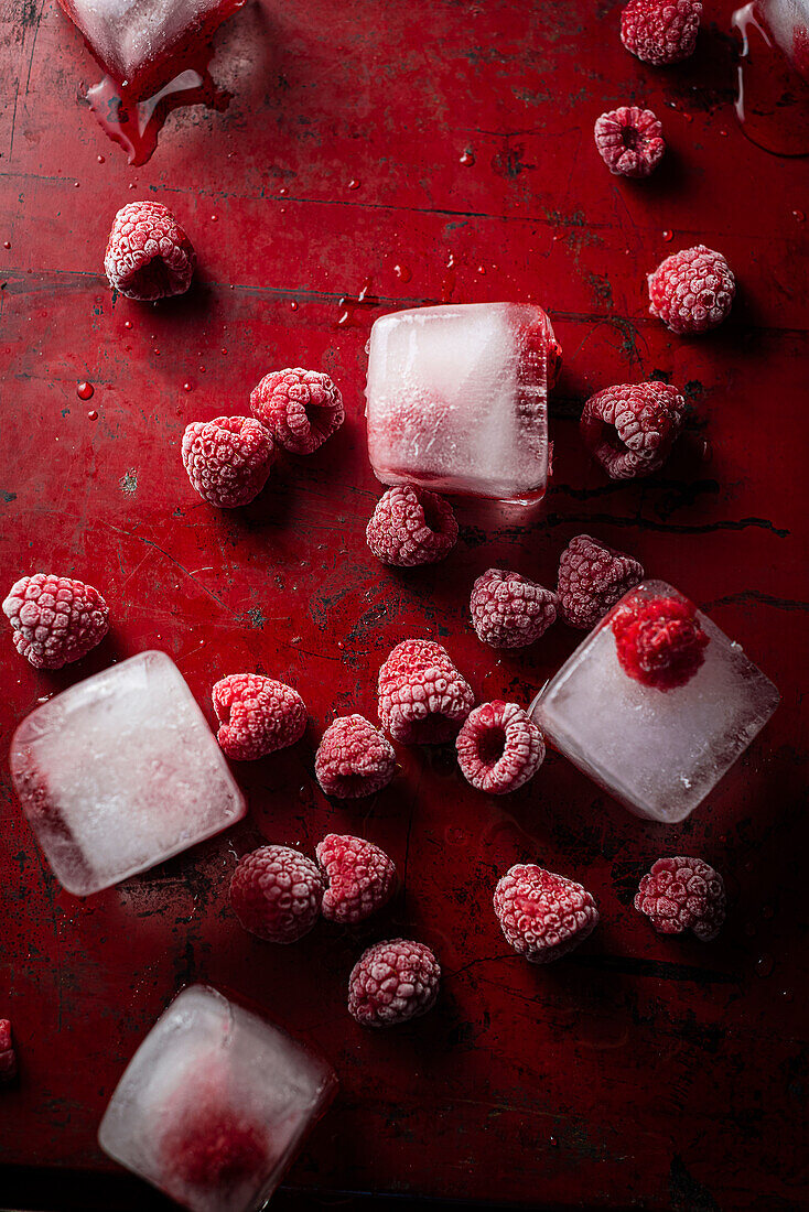 Frozen raspberries and ice cubes on a red background
