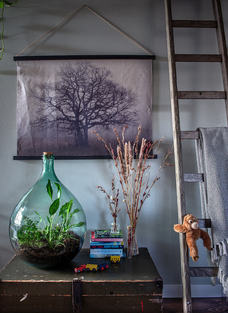 Wall decoration with nature picture, glass vase with plants and books on a chest