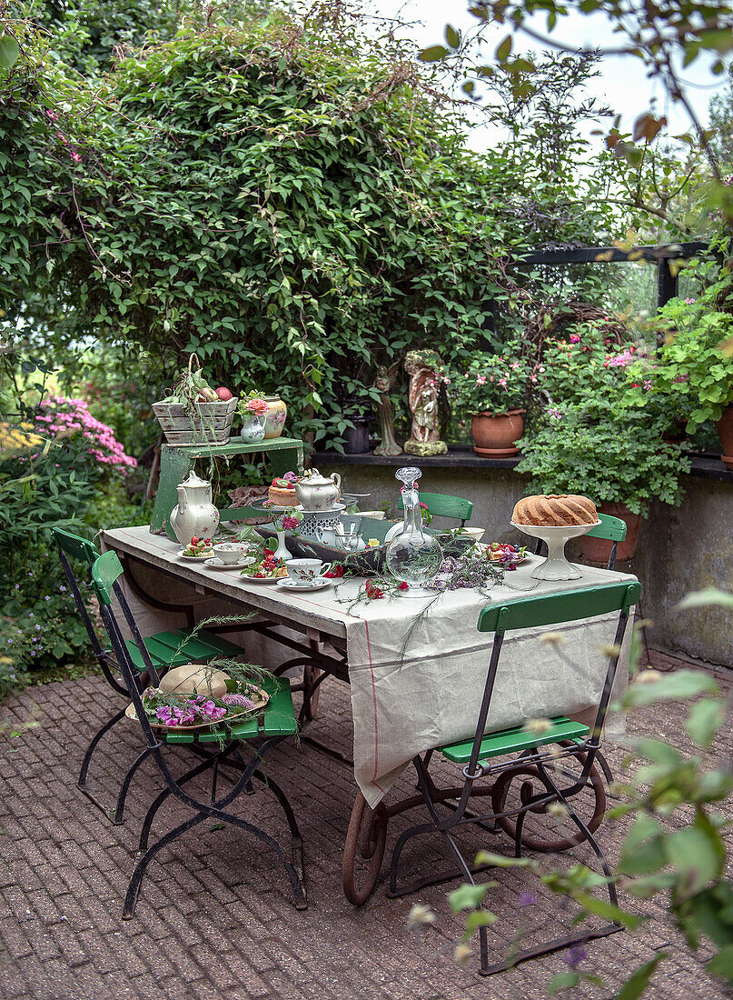 Reich gedeckter Gartentisch mit grünen Metallstühlen