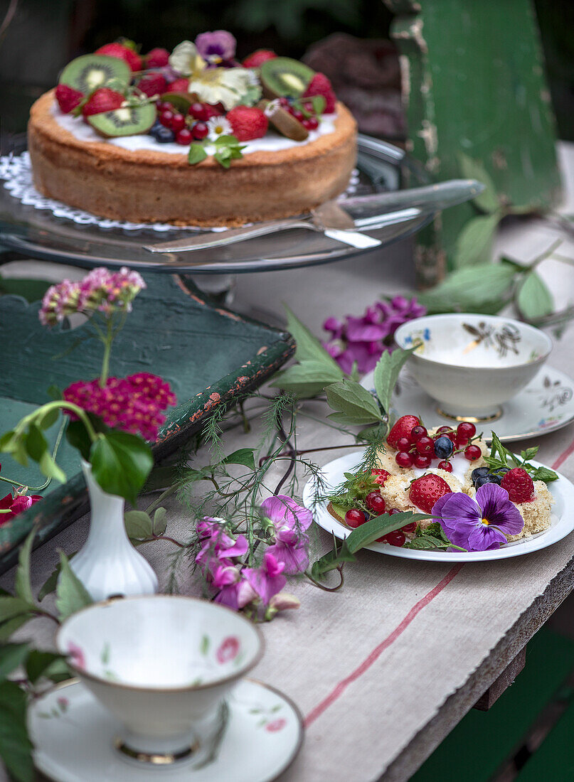 Summer cake with berries and kiwi on a rustic table with floral decorations